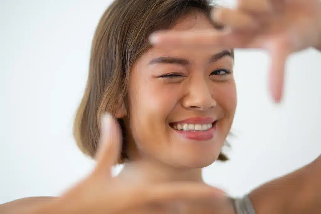 Smiling Asian woman looking at camera and making frame gesture